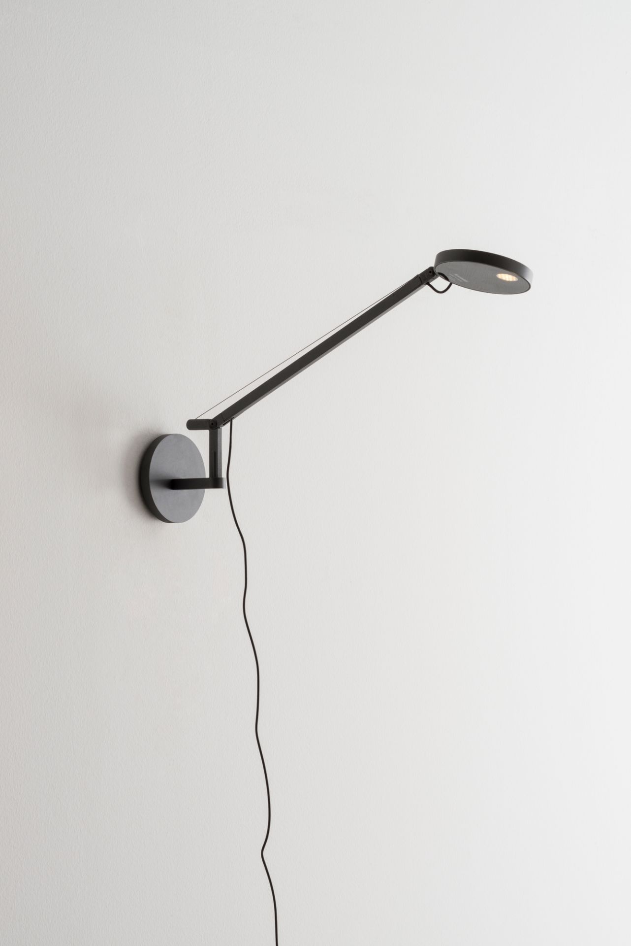 Schwarze Demetra Micro Wandleuchte von Artemide mit verstellbarem Arm und warmweißem Licht.